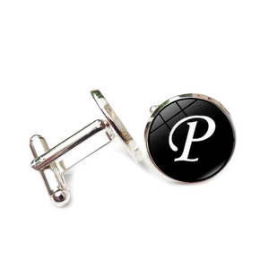 Detailed view of silver cufflink with glass dome and white script letter P on black background
