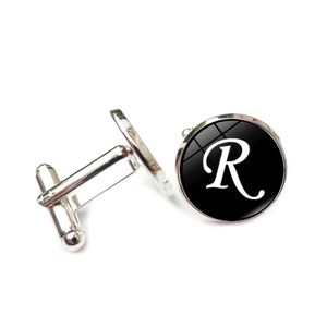 Close-up of silver men's cufflink with a black round base and white letter R detail