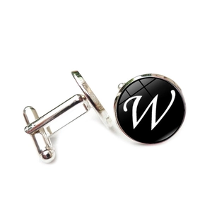 Detail view of silver cufflinks with black background and white script letter W glass dome