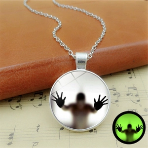 Glow in the dark Halloween glass pendant necklace with a silhouette over vintage sheet music