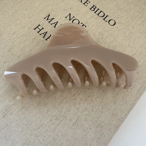 Detail of large creamy coffee hair claw clip on beige fabric, showing glossy resin finish