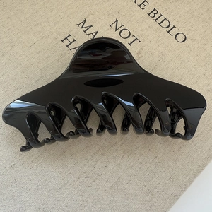 Close-up of a large glossy black claw clip featuring interlocked teeth on a beige fabric