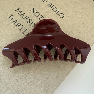 Macro detail of glossy wine red large hair claw clip on a minimalist textured book
