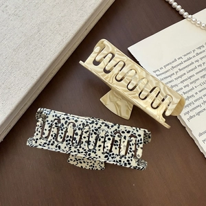 Detail of cream marble and dalmatian print acetate hair claws on a vintage wooden surface
