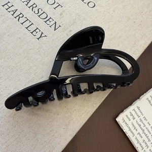 Macro shot of large glossy black shark hair clip showing the smooth finish and metal spring