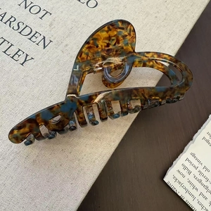 Detailed close-up of large acetate hair claw clip with amber marble texture and heart cutout