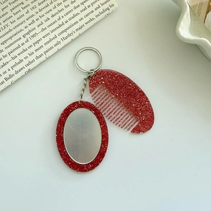 Detail view of a glittery red portable mini comb and oval mirror keychain accessory set