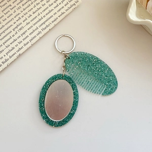 Detail of glitter green oval mirror and comb keychain set on a vintage newspaper background