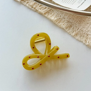 Détail d'une pince à cheveux jaune moutarde avec pois rouges et ressort doré au style ruban