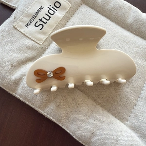 Vue détaillée d'une pince à cheveux crème en acétate avec nœud marron et strass étincelant