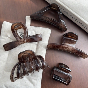 Five assorted leopard print tortoise shell hair claws on a wooden table with fabric bag