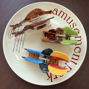 Three creative animal hair claws including a cat and parrot made of acetate on a plate