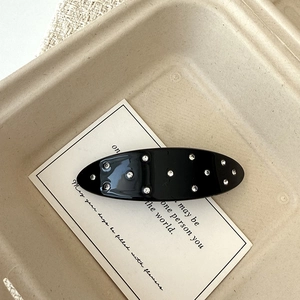 Macro detail of glossy black oval hair clip with silver rhinestones on a beige tray