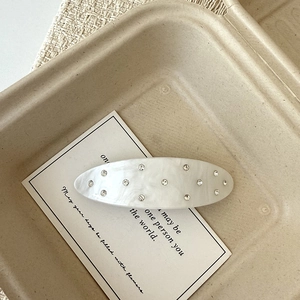 Macro detail of oval acetate hair clip with moonlight white texture and sparkling rhinestones