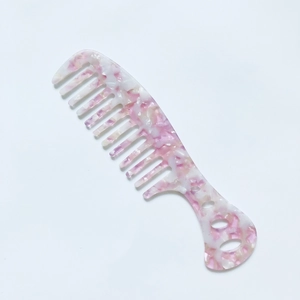 Macro detail of wide-tooth comb in pink marble acetate with decorative cutout handle