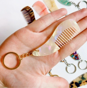 Mini porte-clés peigne en acétate avec effet nacré et anneau doré tenu en main