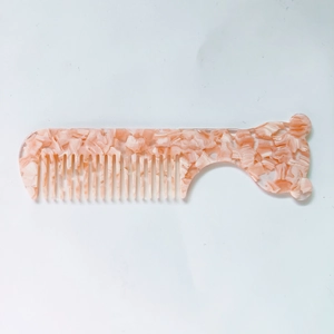 Détail d'un peigne en acétate marbré rose à dents larges avec manche en forme d'ours