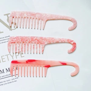 Detailed view of three wide-tooth acetate combs with hooks in various pink textures