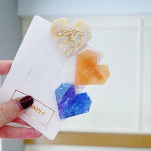 Close-up of three acetate heart hair clips with elegant marble textures in neutral colors