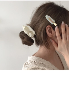 Detail view of acetate pearlescent hair clip and white scrunchie on model
