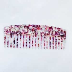 Detail of a wide-tooth acetate hair comb with red and purple floral marble texture
