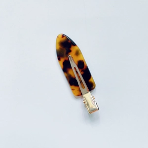 Detailed macro view of tortoiseshell acetate hair clip with golden metal duckbill clamp