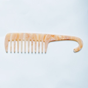 Detail of wide-tooth hair comb with orange and white marble acetate texture and hook handle