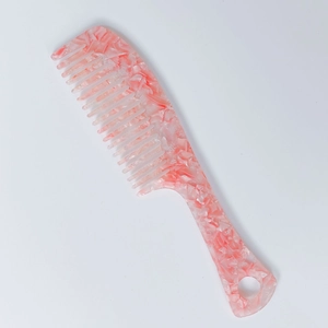 Macro detail of wide-tooth hair comb featuring pink marble acetate and ergonomic handle