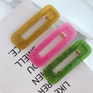 Dettaglio di tre fermagli rettangolari glitterati nei colori oro, rosa e verde su carta