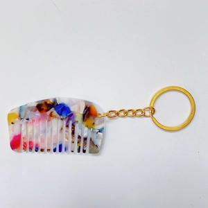Detail van mini acetaat kam sleutelhanger met kleurrijke marmertextuur en gouden ring