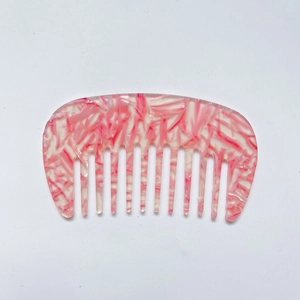 Macro view of pink marble acetate wide-tooth hair comb with smooth curved design