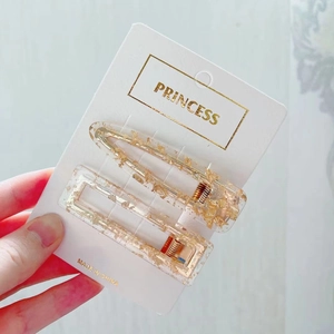 Detail showing two transparent acrylic hair clips with gold foil on a display card