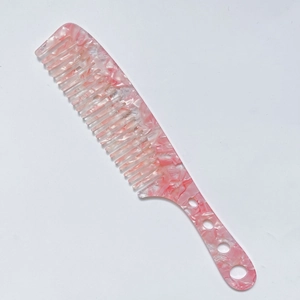 Detail of pink marble acetate hair comb with wide teeth and circular cutouts