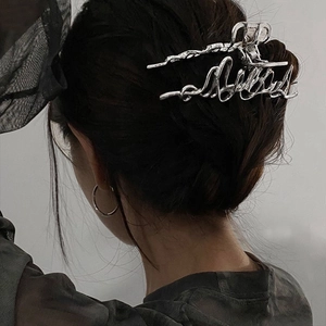 Détail d'une pince à cheveux en métal argenté avec motif de lettres sur un chignon