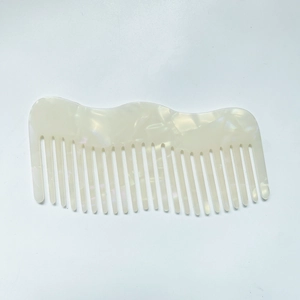 Macro detail of elegant pearl white acetate wide-tooth hair comb with wave design