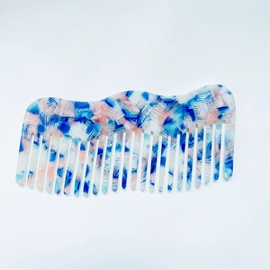 Macro shot of a wavy wide-tooth comb featuring blue and pink marble acetate patterns