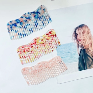Three acetate hair combs with marble patterns in blue, yellow and pink on a magazine background