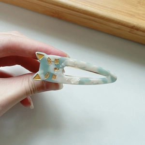 Light blue and white cat-shaped hair clip made of marbled acetate with golden accents