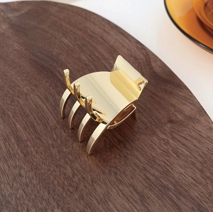 Close-up of a polished gold metal hair claw clip resting on a premium wooden tray