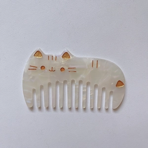 Detail of cute cat shaped acetate hair comb with pearlescent finish and golden engraving