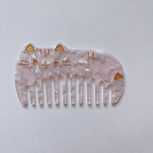 Peine de acetato rosa jaspeado con forma de gato, dientes anchos y detalles faciales dorados