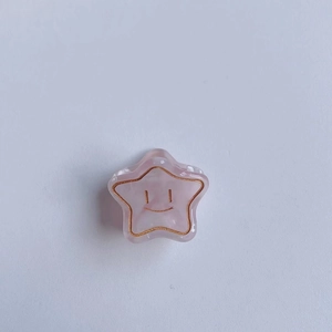 Détail d'une pince à cheveux étoile rose en acétate avec visage souriant et bords dorés