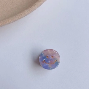Dettaglio del fermaglio per capelli tondo con trama marmorizzata viola e smiley dorato