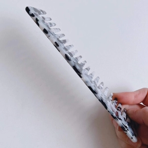 Detail view of wide-tooth acetate comb with marble pattern being held by hand