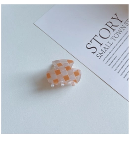 Vue détaillée d'une pince à cheveux à damier orange et blanc en finition acrylique