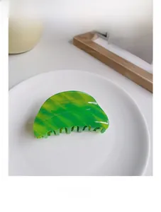 Detail showing green marble acetate hair claw clip with large teeth on a ceramic plate