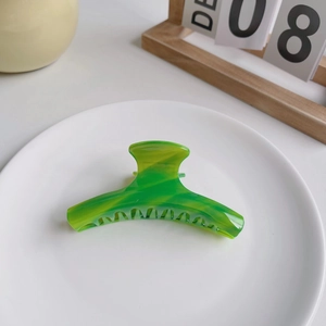 Elegant green and yellow marble acetate hair claw clip for women on a ceramic display