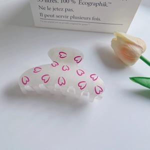 Detail of white frosted hair claw clip featuring pink heart patterns and sturdy teeth