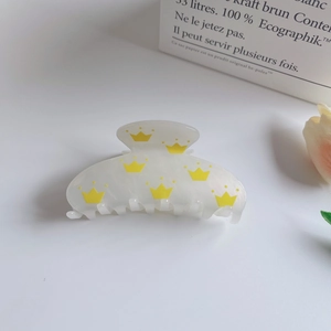 Detail of a pearlescent white hair claw clip with yellow crown prints and sturdy grip