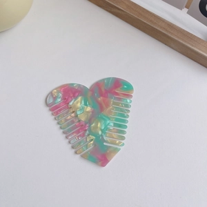 Pink heart-shaped acetate hair comb with marble pattern texture on a minimalist surface
